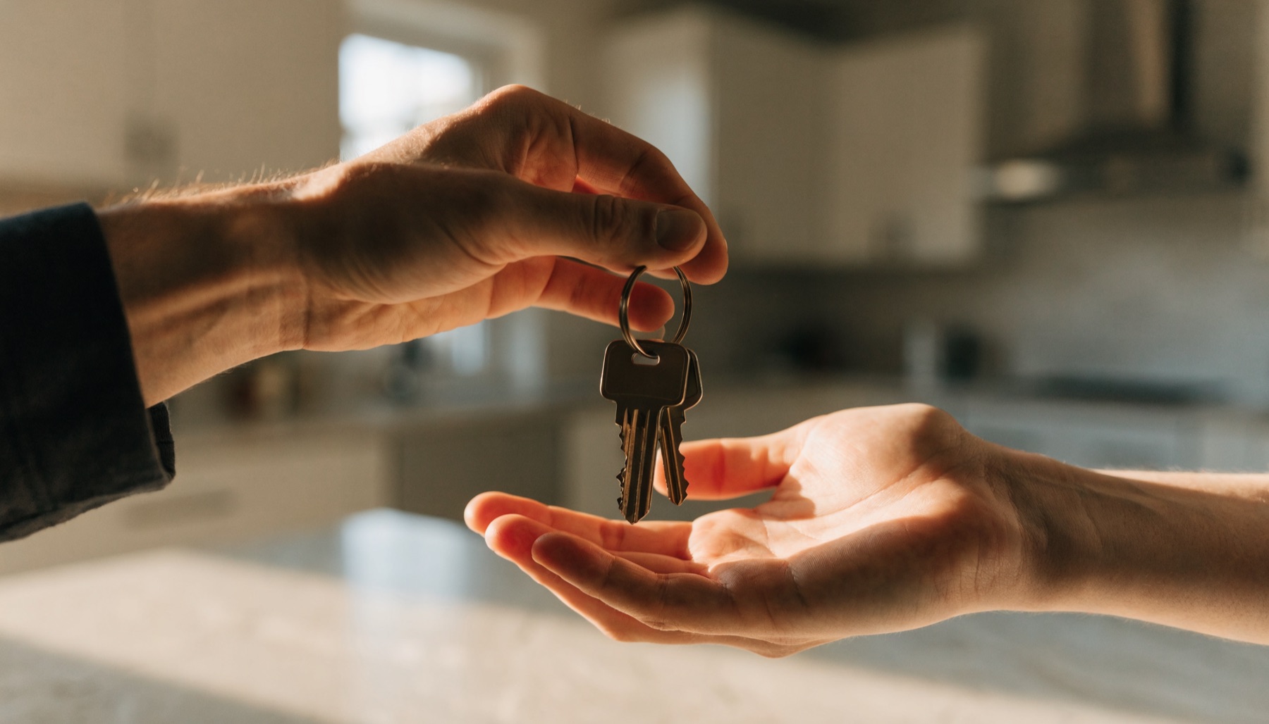 House keys being handed over on a kitchen benchtop after settlement